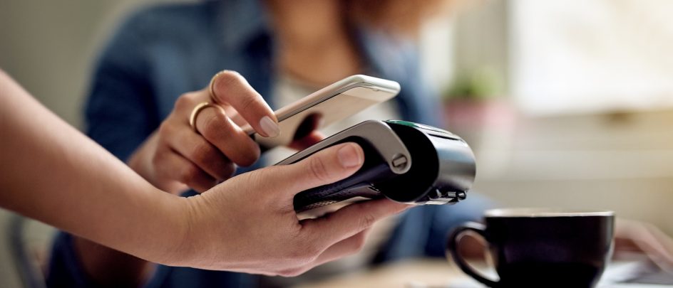 Dame betaler med mobilen. Hun har brunt krøllete hår og en blå skjorte.